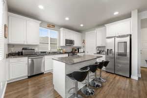 Kitchen with dark hardwood / wood-style flooring, dark stone counters, stainless steel appliances, white cabinets, and a center island