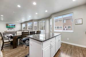 Kitchen featuring white cabinetry, a center island, a wealth of natural light, dark hardwood / wood-style flooring, and dark stone counters