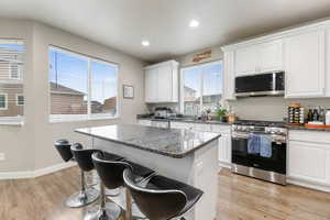 Kitchen with white cabinets, a kitchen island, dark stone countertops, and appliances with stainless steel finishes