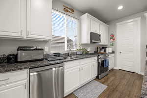 Kitchen with dark stone counters, stainless steel appliances, dark wood-type flooring, sink, and white cabinets