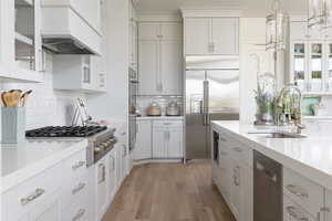 Kitchen featuring white cabinets, sink, light hardwood / wood-style flooring, decorative light fixtures, and stainless steel appliances