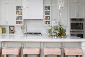 Kitchen with a kitchen bar, decorative backsplash, stainless steel double oven, and decorative light fixtures