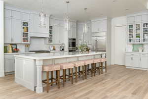 Kitchen with a breakfast bar area, a kitchen island with sink, hanging light fixtures, and light wood-type flooring