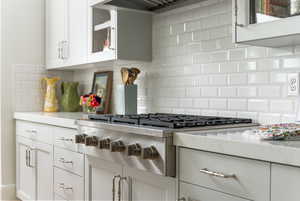 Kitchen featuring decorative backsplash, light stone countertops, custom exhaust hood, white cabinetry, and stainless steel gas stovetop