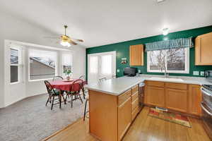 Kitchen with kitchen peninsula, appliances with stainless steel finishes, ceiling fan, sink, and light hardwood / wood-style floors