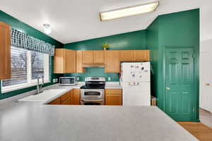 Kitchen with light brown cabinetry, white appliances, vaulted ceiling, sink, and light hardwood / wood-style flooring