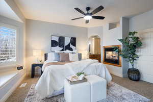 Carpeted bedroom featuring a multi sided fireplace and ceiling fan