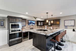 Kitchen featuring hanging light fixtures, wine cooler, kitchen peninsula, appliances with stainless steel finishes, and dark brown cabinetry