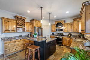 Kitchen featuring dark stone counters, sink, hanging light fixtures, appliances with stainless steel finishes, and a kitchen island