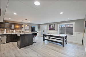 Kitchen with a breakfast bar, hanging light fixtures, dark brown cabinets, a kitchen island, and light stone counters