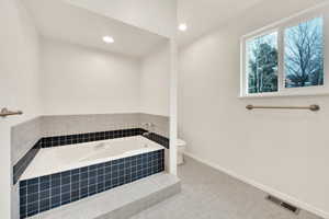 Bathroom with tile patterned floors, a relaxing tiled tub, and toilet