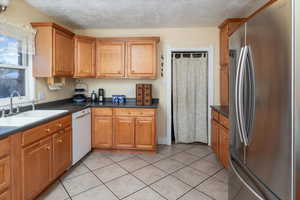 Kitchen with dishwasher, a textured ceiling, stainless steel refrigerator, and sink