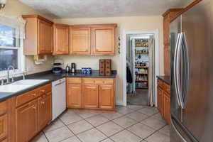 Kitchen with sink, stainless steel fridge, white dishwasher, a textured ceiling, and light tile patterned floors