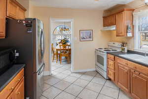 Kitchen featuring sink, light tile patterned floors, a notable chandelier, white electric range oven, and stainless steel refrigerator