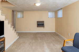 Basement with light carpet, a textured ceiling, and heating unit