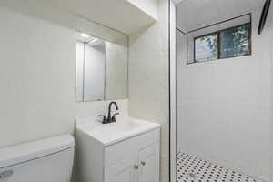 Bathroom featuring tiled shower, vanity, and toilet