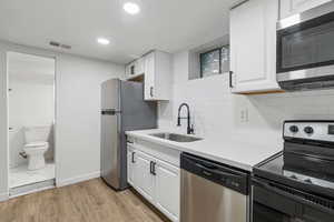 Kitchen featuring white cabinets, sink, light hardwood / wood-style flooring, decorative backsplash, and stainless steel appliances