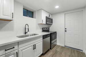 Kitchen with appliances with stainless steel finishes, light hardwood / wood-style floors, white cabinetry, and sink