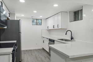 Kitchen with sink, light wood-type flooring, appliances with stainless steel finishes, white cabinetry, and kitchen peninsula