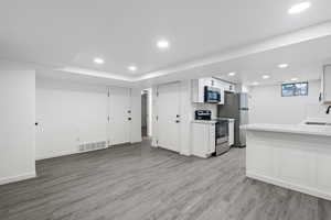 Kitchen with sink, white cabinetry, light hardwood / wood-style floors, kitchen peninsula, and stainless steel appliances