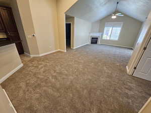 Unfurnished living room featuring ceiling fan, light colored carpet, a fireplace, and vaulted ceiling