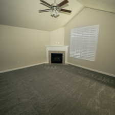 Unfurnished living room featuring dark colored carpet, ceiling fan, a tile fireplace, and vaulted ceiling