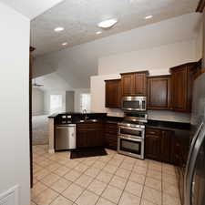 Kitchen featuring ceiling fan, sink, vaulted ceiling, light tile patterned flooring, and appliances with stainless steel finishes