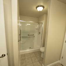 Bathroom with tile patterned floors, a shower with door, a textured ceiling, and toilet