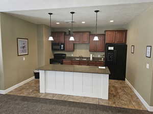 Kitchen featuring a textured ceiling, a center island, black appliances, and decorative light fixtures