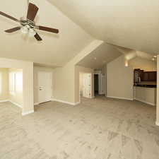 Unfurnished living room with ceiling fan, light colored carpet, lofted ceiling, and a textured ceiling