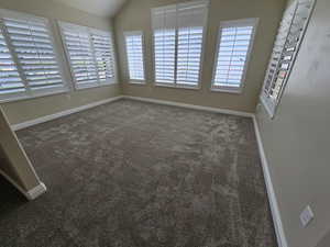 Empty room with vaulted ceiling and dark colored carpet