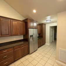 Kitchen featuring stainless steel fridge, dark stone counters, lofted ceiling, and light tile patterned flooring