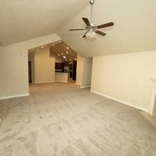 Unfurnished living room featuring carpet floors, vaulted ceiling, ceiling fan, and a tiled fireplace