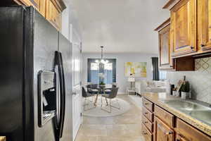 Kitchen featuring sink, decorative light fixtures, black refrigerator with ice dispenser, light tile patterned floors, and backsplash