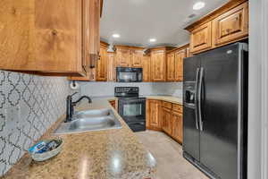 Kitchen with decorative backsplash, light tile patterned floors, sink, and black appliances