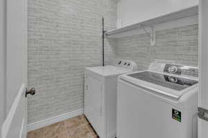 Clothes washing area with separate washer and dryer and brick wall