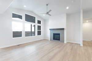 Unfurnished living room featuring ceiling fan, a fireplace, vaulted ceiling, and light wood-type flooring