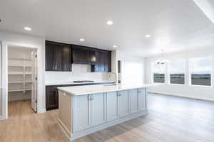 Kitchen with a center island with sink, hanging light fixtures, custom range hood, and gas cooktop