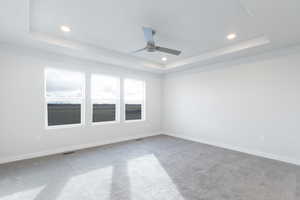 Unfurnished room featuring carpet flooring, ceiling fan, and a raised ceiling