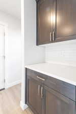 Bar featuring dark brown cabinetry, decorative backsplash, and light hardwood / wood-style flooring