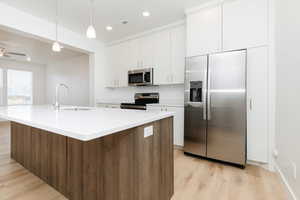 Kitchen with white cabinetry, sink, hanging light fixtures, an island with sink, and appliances with stainless steel finishes