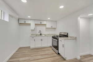 Downstairs kitchen with stainless steel range with gas cooktop, sink, white cabinets, and light hardwood / wood-style flooring