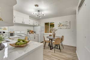 Kitchen with white cabinetry, light stone counters, white appliances, and light hardwood / wood-style floors