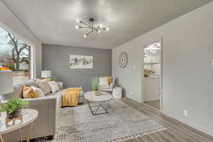 Living room featuring a textured ceiling, light wood-type flooring, an inviting chandelier, and wooden walls