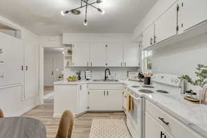 Kitchen with white range with electric stovetop, white cabinetry, sink, and a textured ceiling