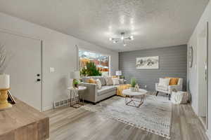 Living room featuring a chandelier, a textured ceiling, light hardwood / wood-style floors, and wood walls