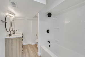 Full basement bathroom with tub / shower combination, a textured ceiling, toilet, vanity, and hardwood / wood-style flooring