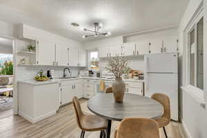 Kitchen featuring white appliances, backsplash, white cabinetry, and sink