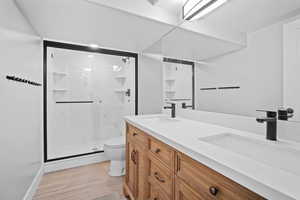 Bathroom featuring toilet, enclosed shower, and double-sink vanity