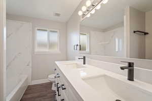 Full bathroom featuring toilet, double sink vanity, cultured marble shower / bathtub combination